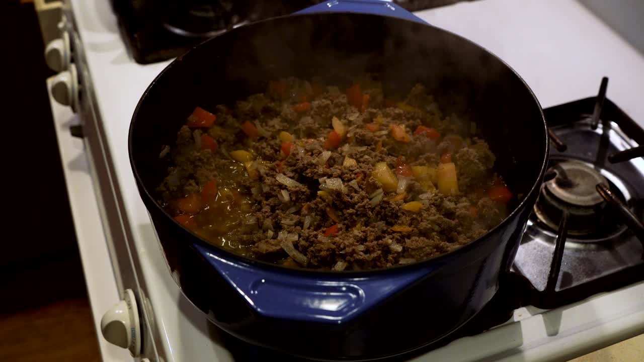 carne molida, cebollas y pimientos cocidos a fuego lento en un horno holandés en una estufa de gas