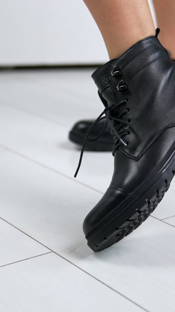 Bare-legged model demonstrating low black leather boots with laces. Woman rises foot to shoe the tractor sole of footwear. Close up.