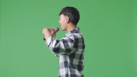 녹색 스크린 배경에서 마이크를 들고 하는 젊은 아시아 십대 소년의 측면 시각
