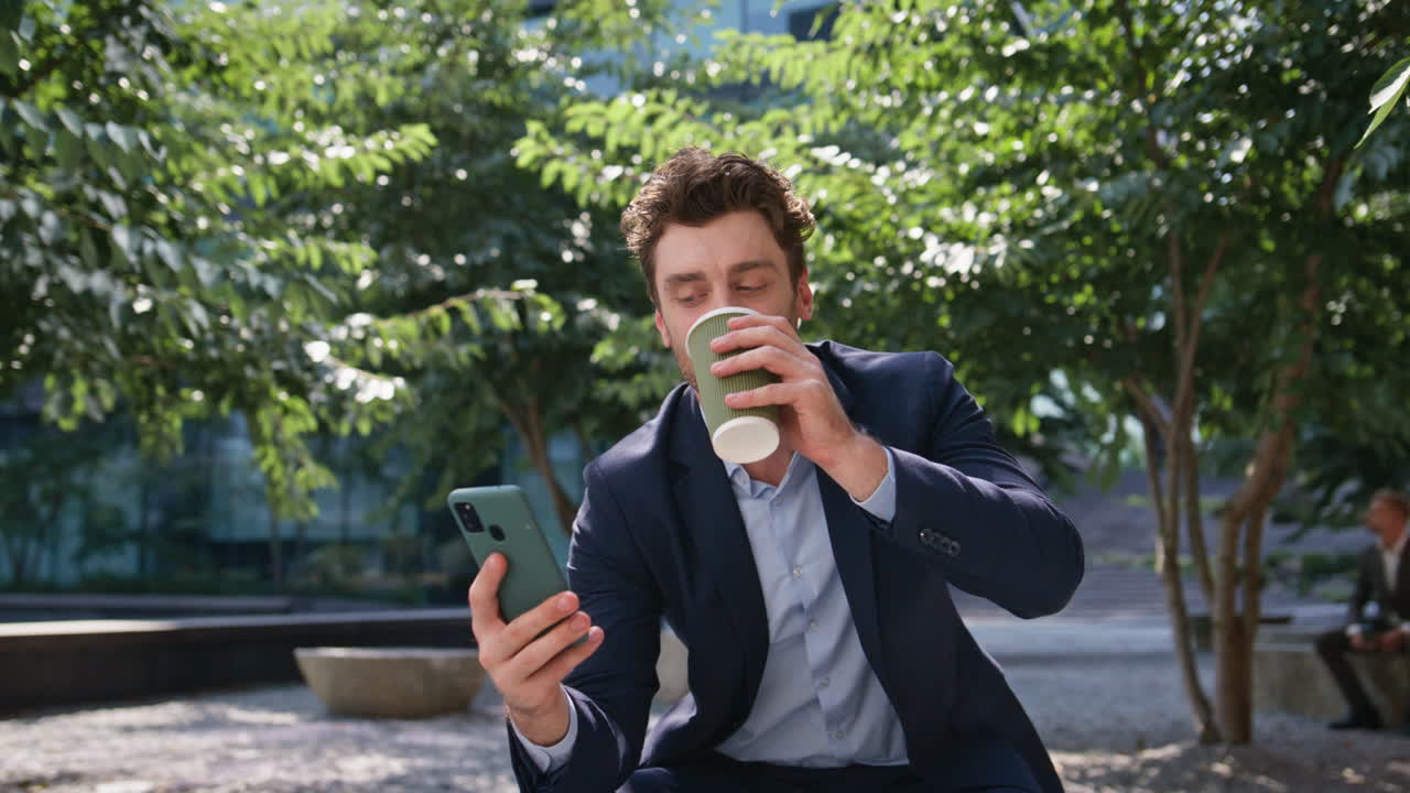 Forretningsmand med kaffe griner af besked, kigger på smartphone på solrig gade, nærbillede.