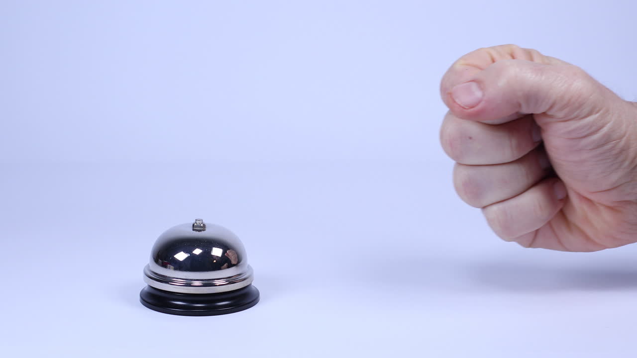 An clenched fist impatiently slams a concierge bell four times in front of a white background