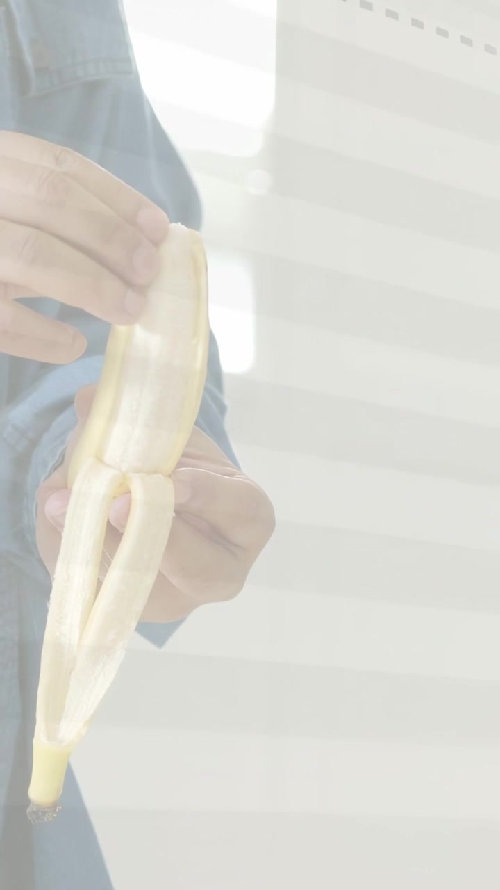 Video verticale: Uomo che sbuccia una banana con la mano destra, ruotando il frutto, preparando del cibo