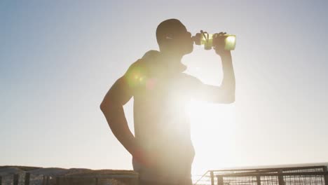 Hombre-Afroamericano-Bebiendo-Agua,-Tomando-Un-Descanso-En-El-Ejercicio-Al-Aire-Libre-Junto-Al-Mar