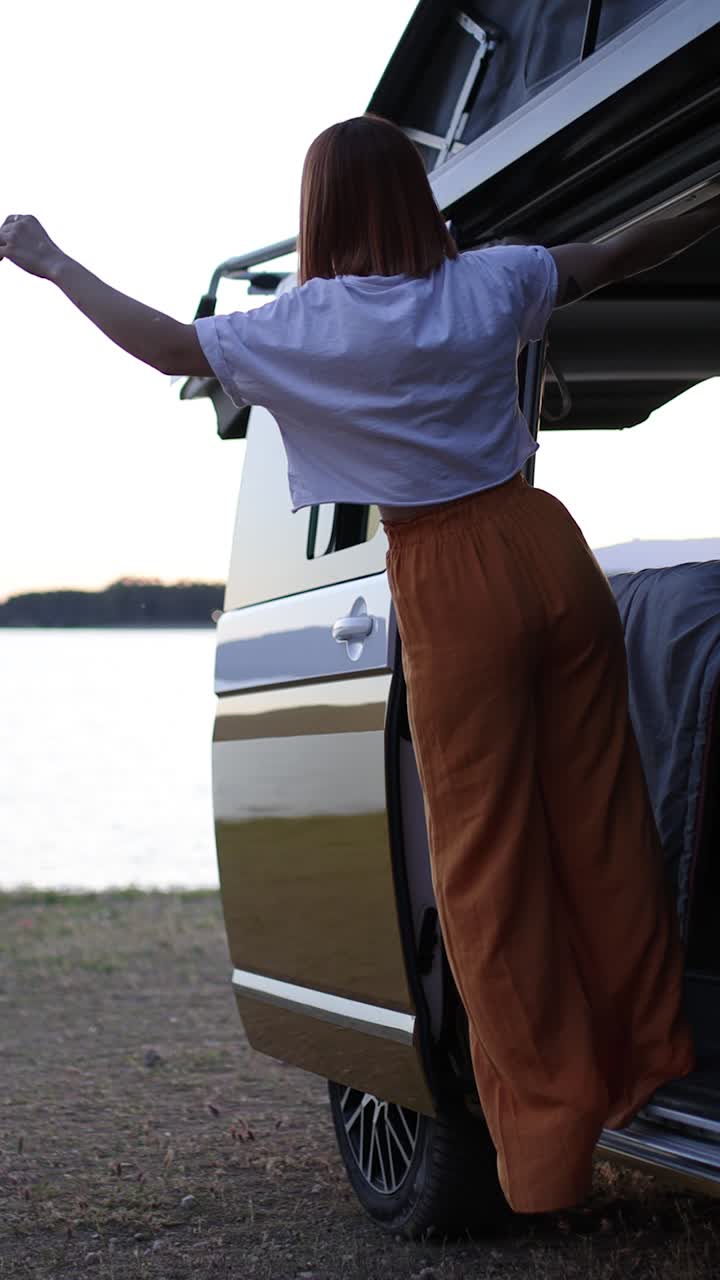 Donna in piedi sulla porta di un camper che guarda il lago.