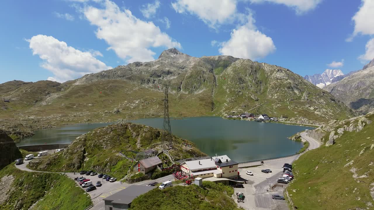 Aerial view of Totensee at Grimsel Pass in the Swiss Alps, showing the turquoise reservoir surrounded by rocky slopes, alpine meadows, and towering peaks