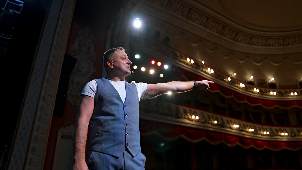 Man in front of theater hall put hand to ear. Actor is standing on stage and talking with public during the performance. Classic theater interior.
