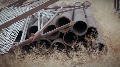 Rostige-Verlassene-Alte-Röhren-Und-Materialien,-Die-Mitten-In-Der-Wüste-Gestrandet-Sind,-Mit-Trockenen-Ästen,-Die-Leicht-Vom-Wind-Bewegt-Werden