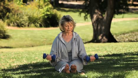 Elderly-woman-working-her-muscles-with-dumbbells-sitting-on-the-grass