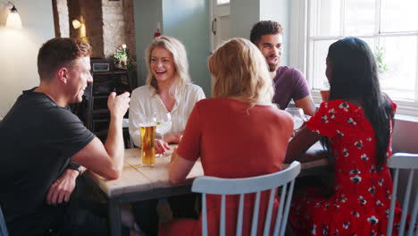 grupo de raza mixta de amigos adultos jóvenes sentados en una mesa en un pub hablando