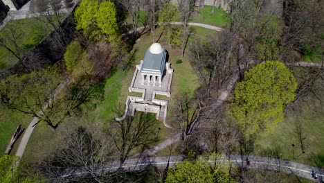 memorial mausoleum of white stone in the sunny, spring park of the city of olomouc, people passing by