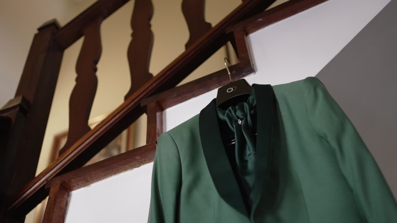 Elegant green groom's wedding suit on a hanger, placed near a wooden staircase