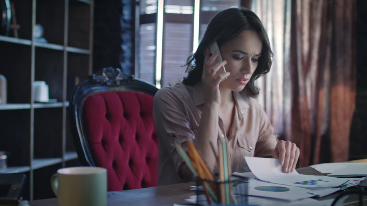 mujer de negocios molesta respondiendo a una llamada móvil mientras trabaja con documentos