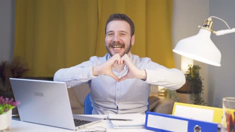 home office worker man makes heart symbol looking at camera.