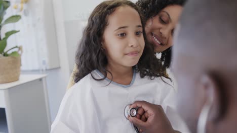 Happy-diverse-doctor-examining-sick-girl-patient-with-stethoscope-with-her-mother-in-slow-motion