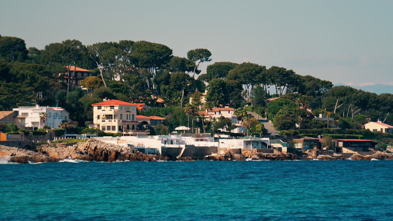 Distant view of multiple villas on the shore with the waves of the sea crashing on the rocks