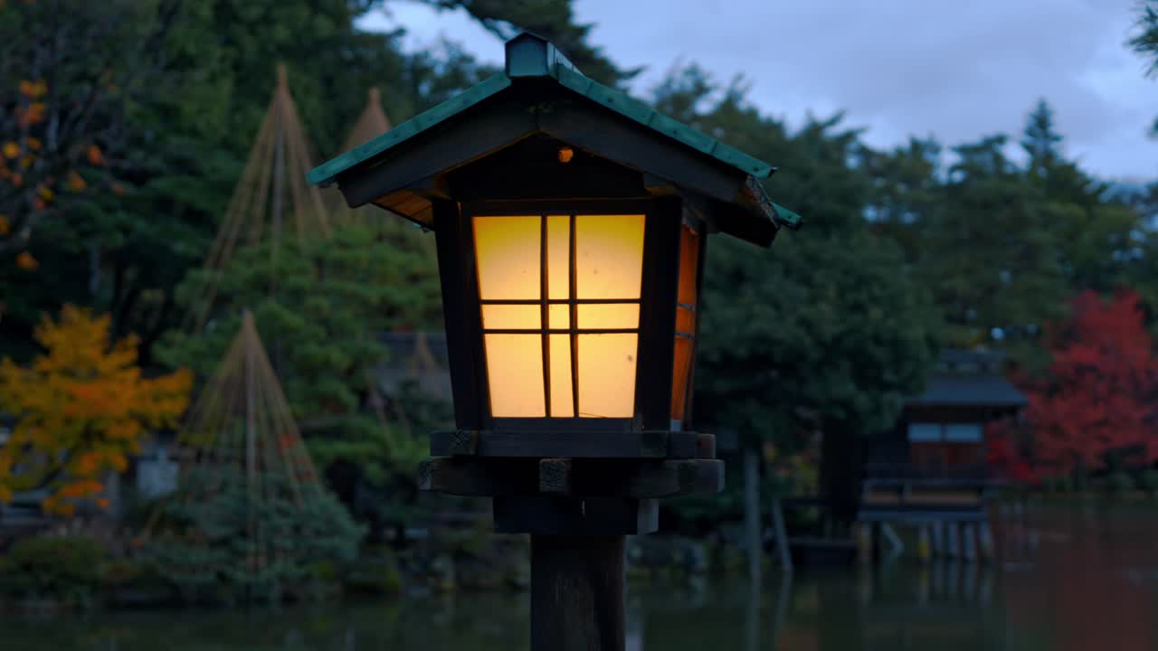 A traditional Japanese lantern glows softly in the night, illuminating the peaceful paths of Kanazawa’s Kenroku-en Gardens.