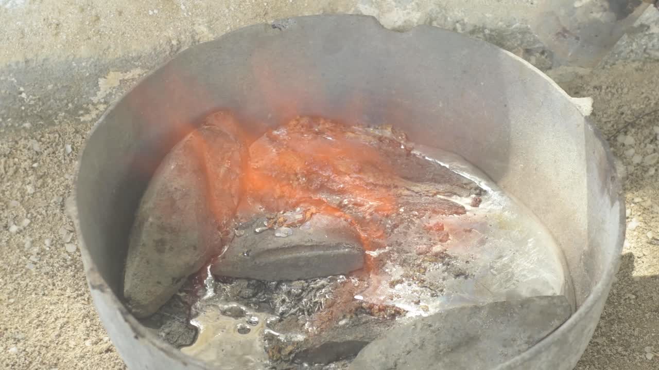 Molten lead in a metal container with fumes rising, industrial setting, close up