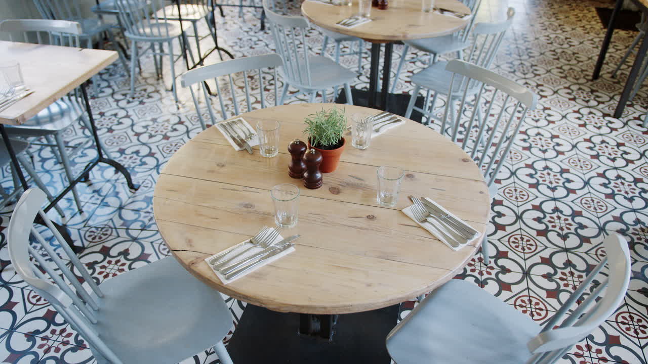 vista portátil elevada centrada en una mesa redonda de madera con asientos y sillas en un comedor vacío de un restaurante, durante el día