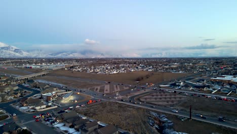 Tráfico-A-Lo-Largo-De-Una-Carretera-En-Una-Comunidad-Suburbana-En-Un-Valle-Debajo-De-Las-Montañas-Rocosas-Nevadas---Vista-Aérea-Descendente