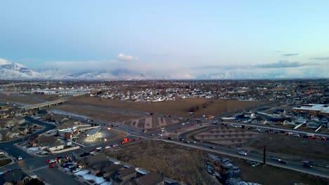 traffic along a highway in a suburban community in a valley beneath the snowy rocky mountains - descending aerial view