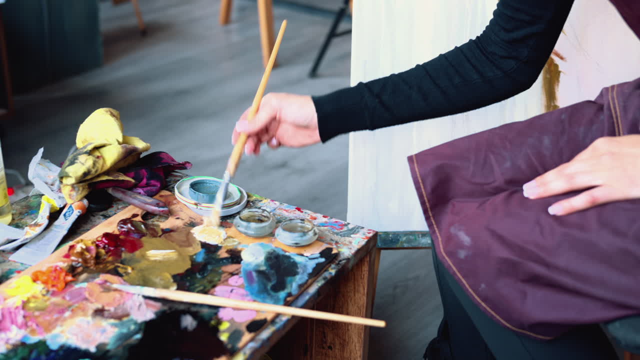 Close up of a woman picking up paint with a brush, from a palette