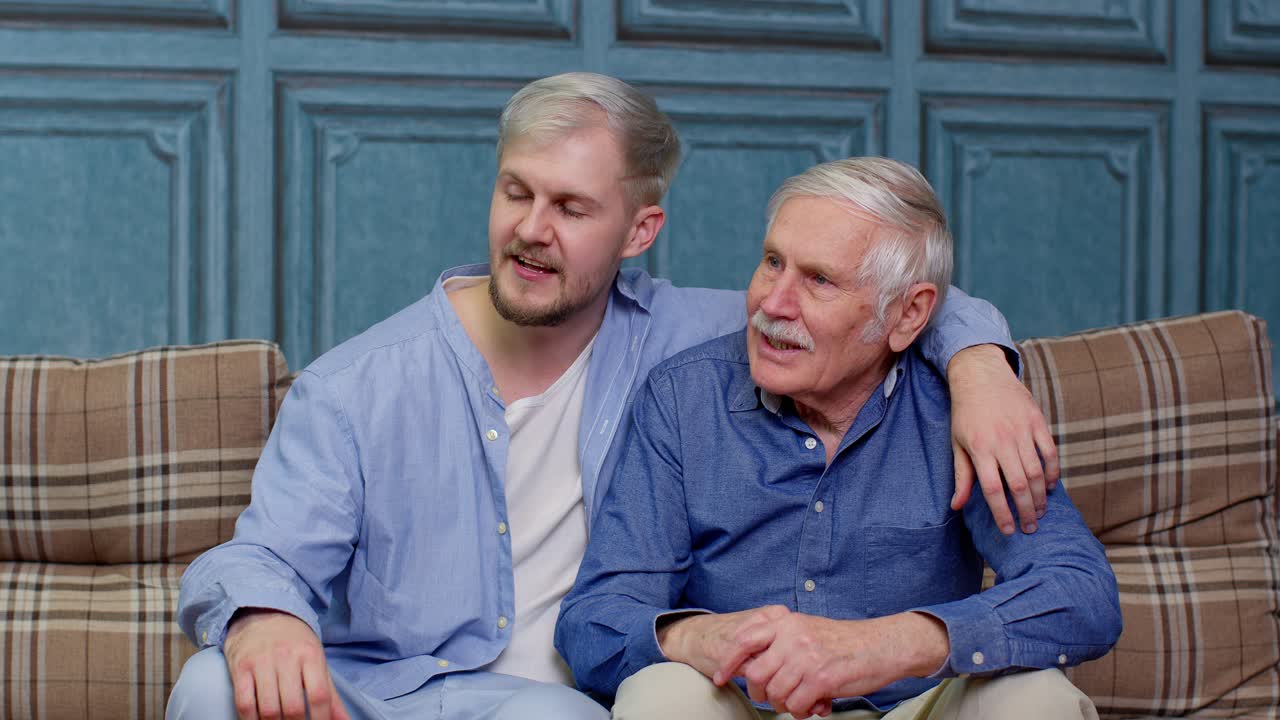 Familie aus Senior-Vater und erwachsenem Sohn oder Enkel unterhält sich, plaudert und entspannt auf dem Sofa.
