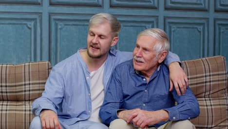 Family-of-senior-father-and-adult-son-or-grandson-having-conversation-chatting-relaxing-on-couch