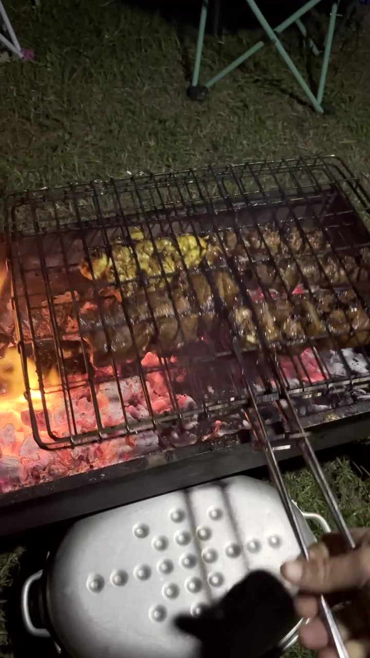 Verticale. POV di un uomo che gira la griglia con spiedini di carne cotti alla brace su carboni ardenti