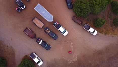 Drohne-Fliegt-Nach-Oben-Und-Schaut-Direkt-Nach-Unten-Auf-Rotes-Quad-ATV-Auf-Unbefestigten-Straßenparkplatz-Und-Macht-Wheelie-Burn-Outs-Im-Dreck-Mit-Autos-Und-Lastwagen-Mit-Anhängern-Und-Outdoor-Abenteuerfahrzeugen