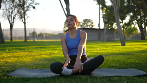 Beautiful-young-woman-sitting-in-lotus-position-on-her-yoga-mat-in-meditation-during-sunrise-in-a-grass-park