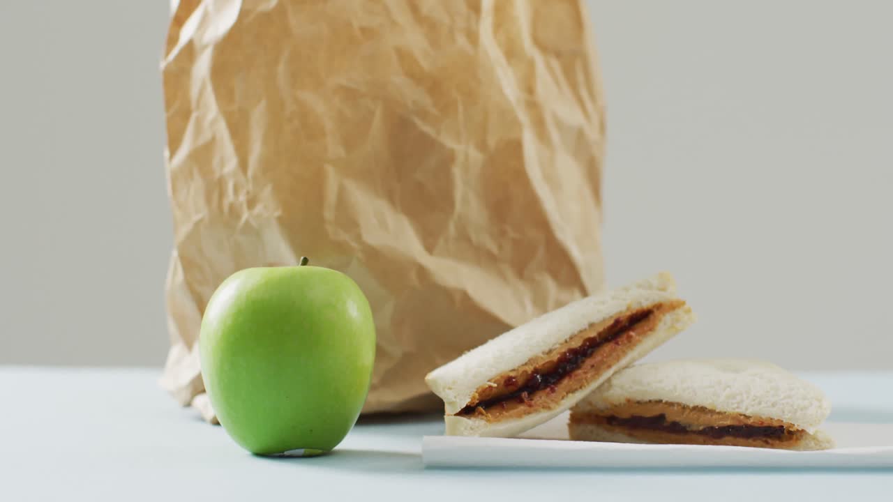 sándwich de mantequilla de maní y jalea con manzana y bolsa de papel contra un fondo blanco