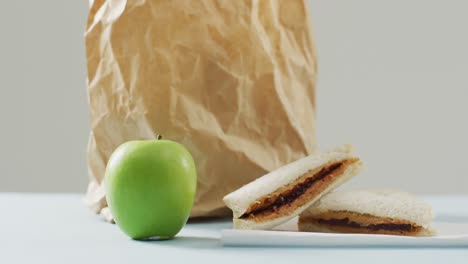 Peanut-butter-and-jelly-sandwich-with-apple-and-paper-bag-against-white-background