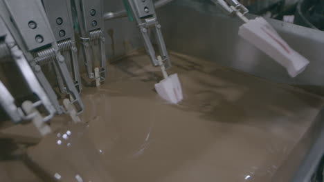 fixed clip from ice cream manufacter's factory, showing ice creams being dipped one by one into melted chocolate