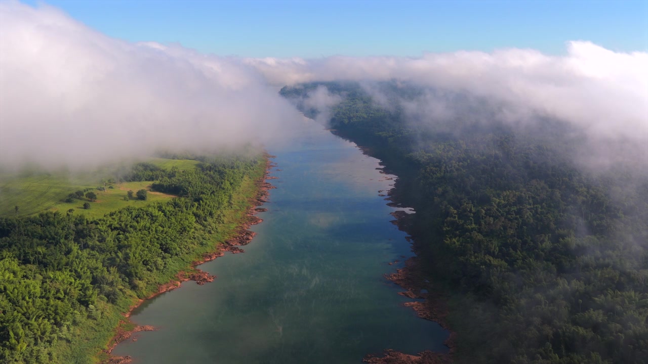 Parana River flows between Misiones, Argentina and Itapua, Paraguay beneath radiation fog bordering Atlantic Forest (Mata Atlantica), slow drone forward flyover.