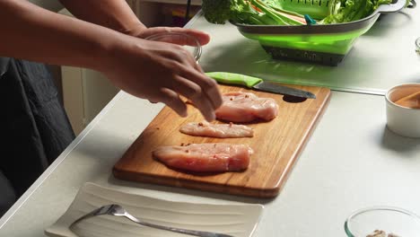 seasoning raw chicken breasts on a cutting board