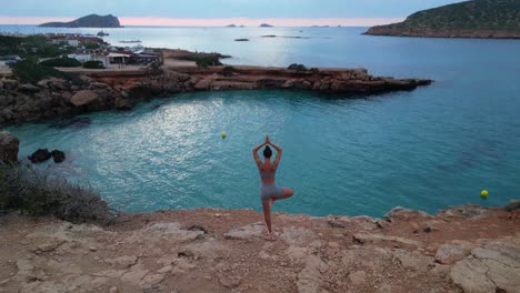 Stunning-aerial-top-view-flight-Yoga-Girl-position-tree-sunset-cliff-beach-island-ibiza-Spain-drone-camera-pointing-down