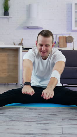 young man doing workout at home. guy is sitting on a mat and trying to do exercising during a quarantine period. difficulties of doing workout at home. vertical video