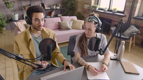 top view of young man and woman wearing headphones sitting at a table with microphones while they recording a podcast 2