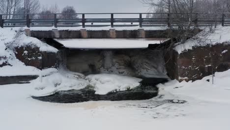 frozen waterfall under small countryside bridge, ice sheet cover on pond