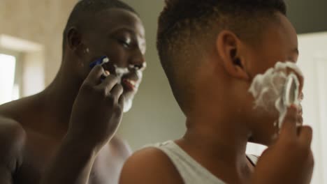 video de un feliz padre y hijo afroamericanos afeitándose en el baño.