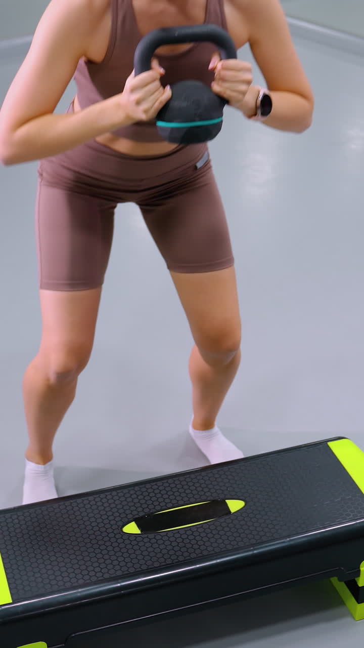 vista de arriba hacia abajo de una mujer en forma realizando ejercicios de entrenamiento de fuerza levantando pesas en un gimnasio moderno, un gran espejo y una alfombra de yoga en el fondo resaltan la intensidad del entrenamiento y la rutina de fitness enfocada