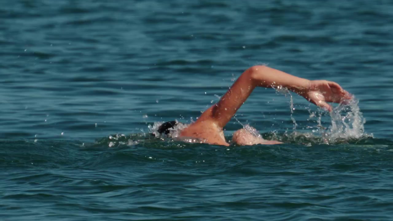 Atleta nadando crol en el agua azul del océano, creando salpicaduras. La escena resalta el movimiento, el deporte y el ejercicio.