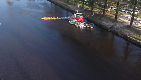 aerial footage captures colorful boats moored along a tranquil riverbank in brunswick heads, nsw, under clear skies
