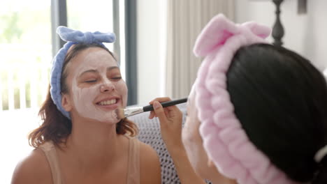 two biracial female friends applying facial masks at home