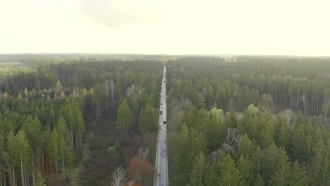 pullback shot of a drone over a autumn colored forest tracking a transporter car while flying backwards with the copter