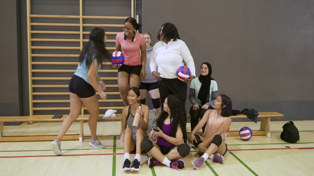 Diverse Teamkolleginnen posieren mit Smartphone-Selfie, halten Volleybälle im Fitnessstudio vor dem Training