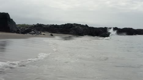 Low-flying-aerial-over-small-waves-at-Skardsvik-beach-with-dark-basalt-cliffs