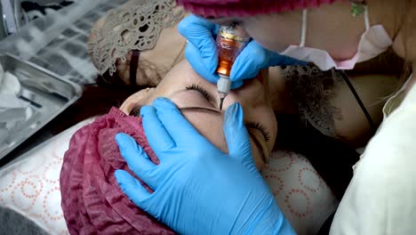en primer plano del procedimiento de microblading, la niña se acuesta en el sofá en el salón de belleza, y una esteticista profesional hace maquillaje permanente de sus cejas.