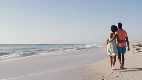 pareja afroamericana abrazándose juntos y caminando por una playa soleada