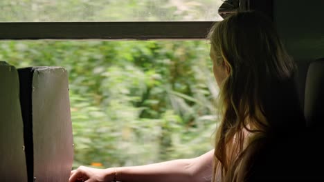 a woman sits peacefully inside a sri lankan train, gazing out the window at the lush green jungle that flanks the iconic ella to kandy railway.